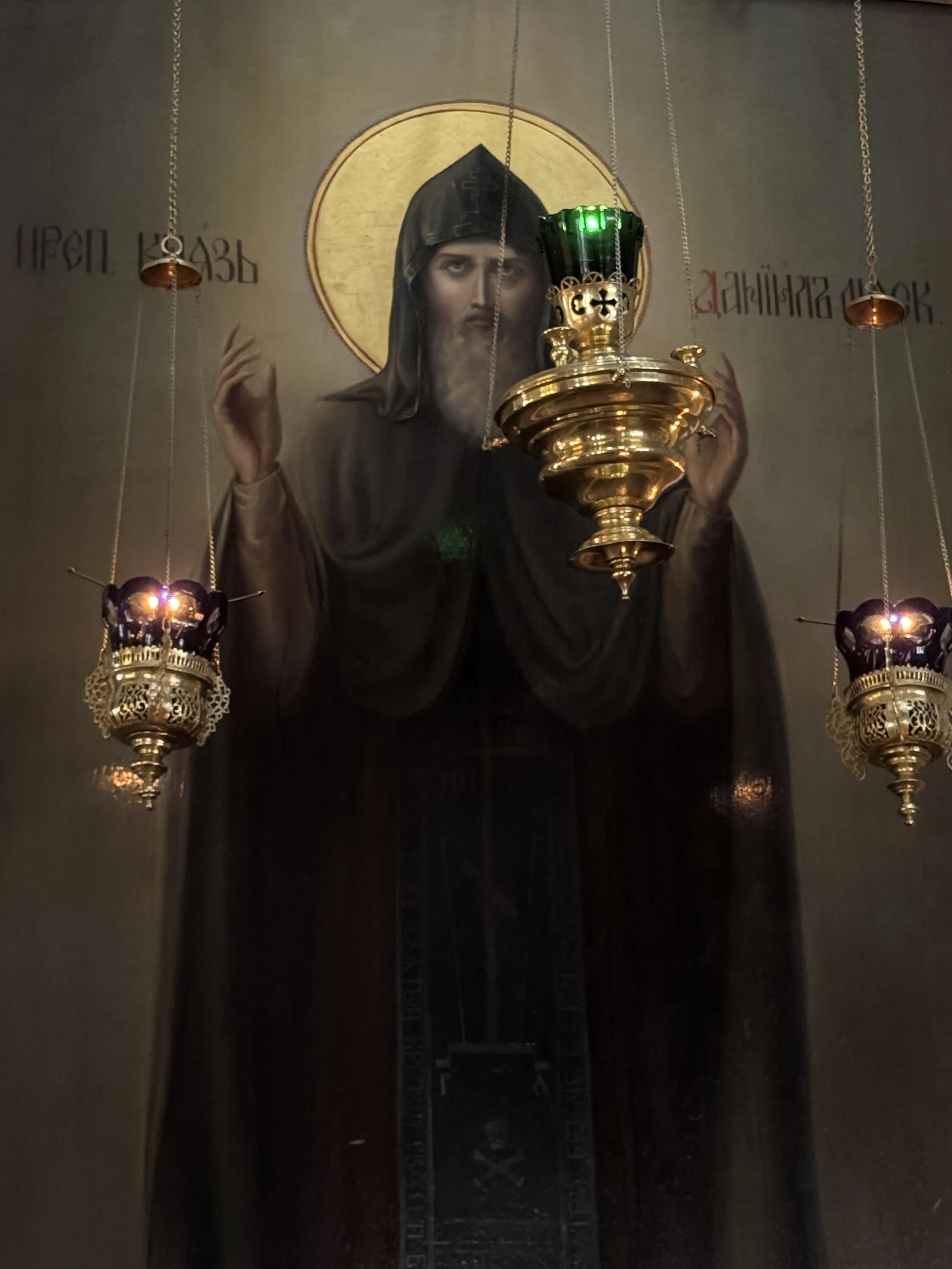 Photograph of Daniel of Moscow’s icon in Danilov Monastery’s Trinity Cathedral; hanging lamps obscure part of the icon, and the photograph omits its outer frame.